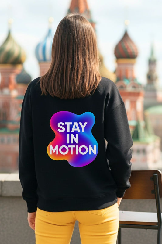 Woman wearing a black oversized sweatshirt with 'Stay in Motion' design, standing in front of a cityscape.