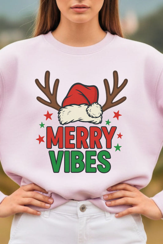 close up of a woman wearing a light baby pink oversized sweatshirt with 'Merry Vibes' design featuring reindeer antlers and a Santa hat.
