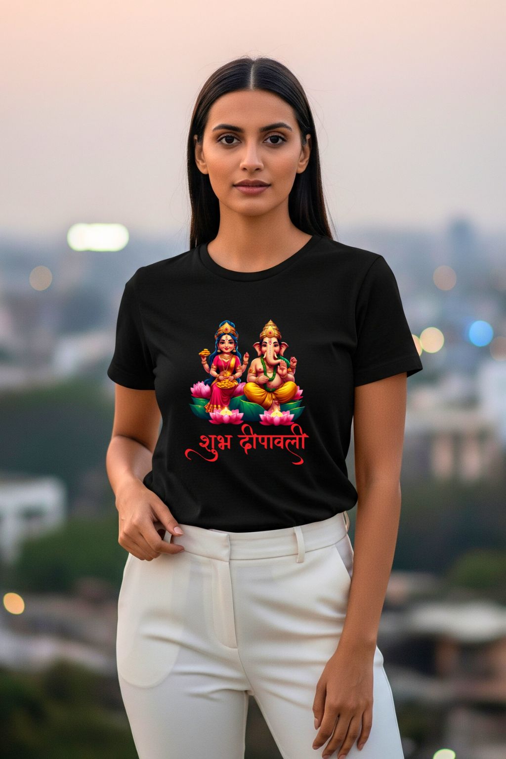 A woman wearing a Lakshmi and Ganesha Divine Duo black t-shirt, with a festive design, standing against a city background.