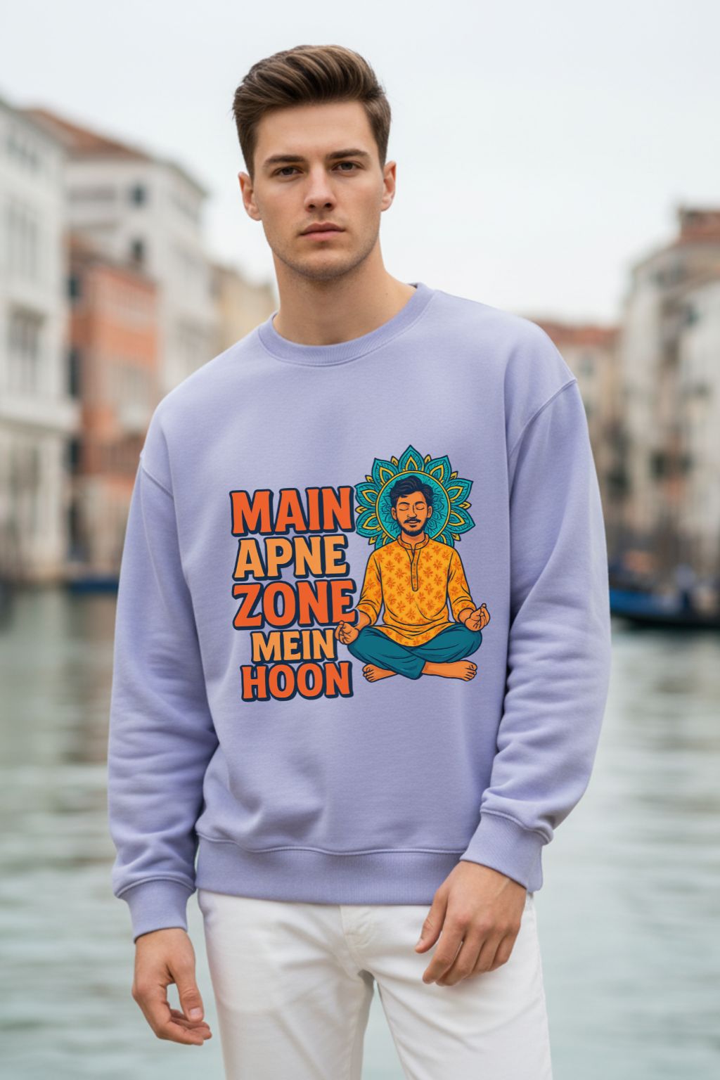 Man wearing a lavendar oversized  sweatshirt with a colorful graphic and text, standing in front of a canal.