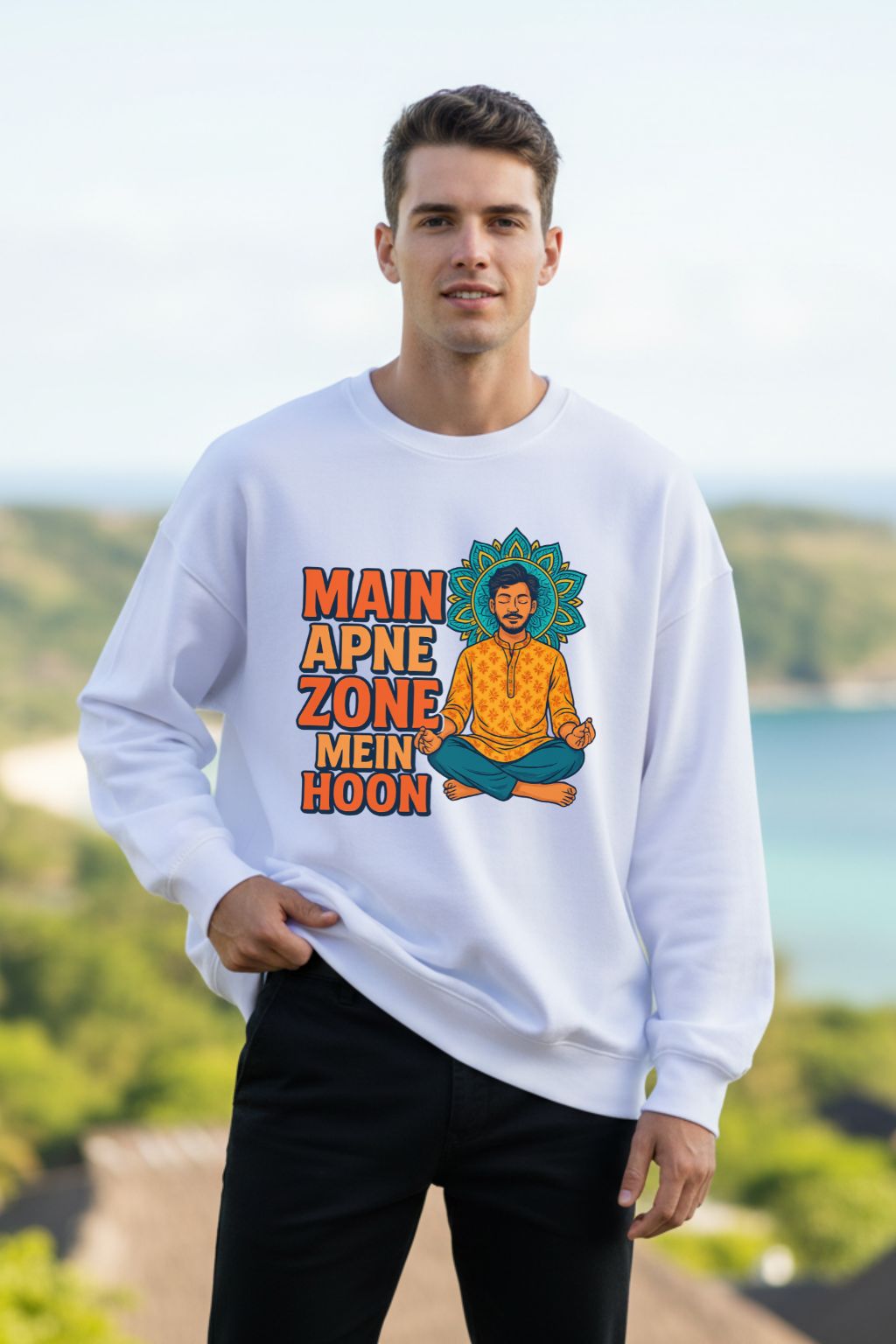 Man wearing a white oversized sweatshirt with a colorful graphic and text, standing outdoors with greenery and water in the background.