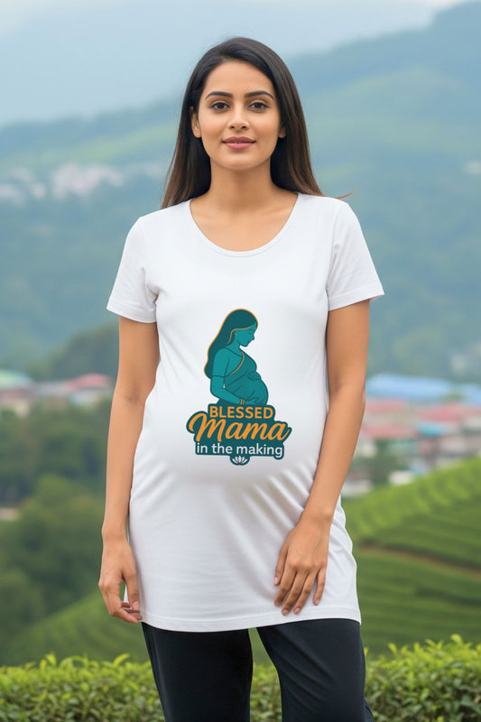 Woman wearing a white maternity dress with a graphic design and text, standing in front of a scenic background.