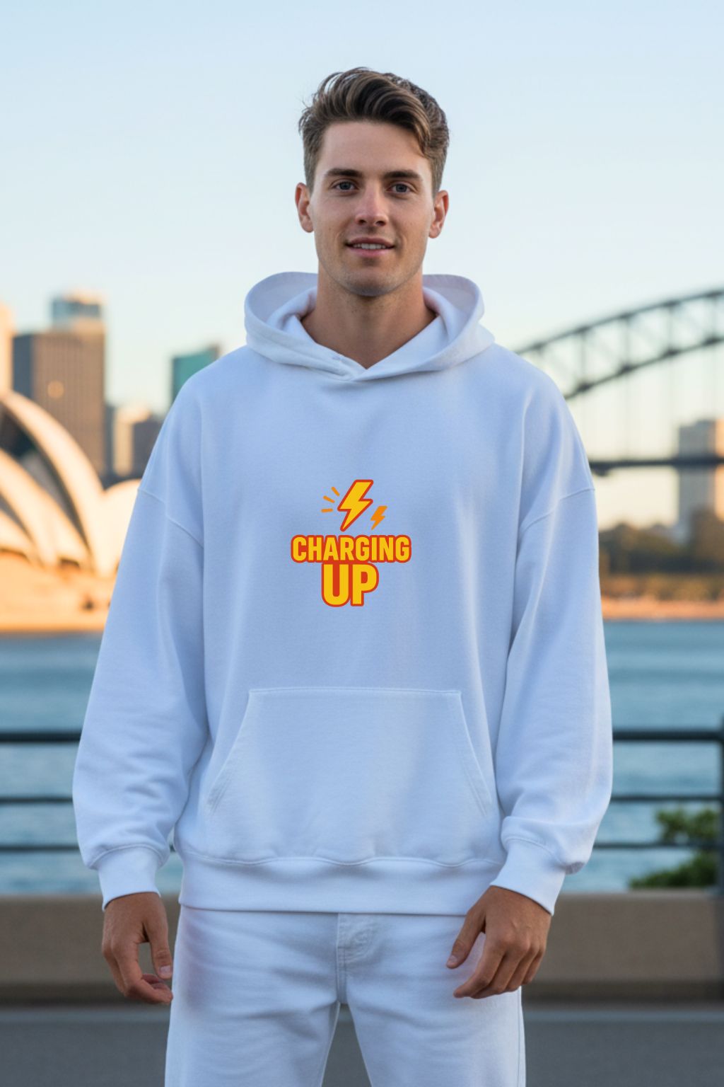 Man wearing a white hoodie with 'Charging Up' text, standing outdoors with a cityscape background.