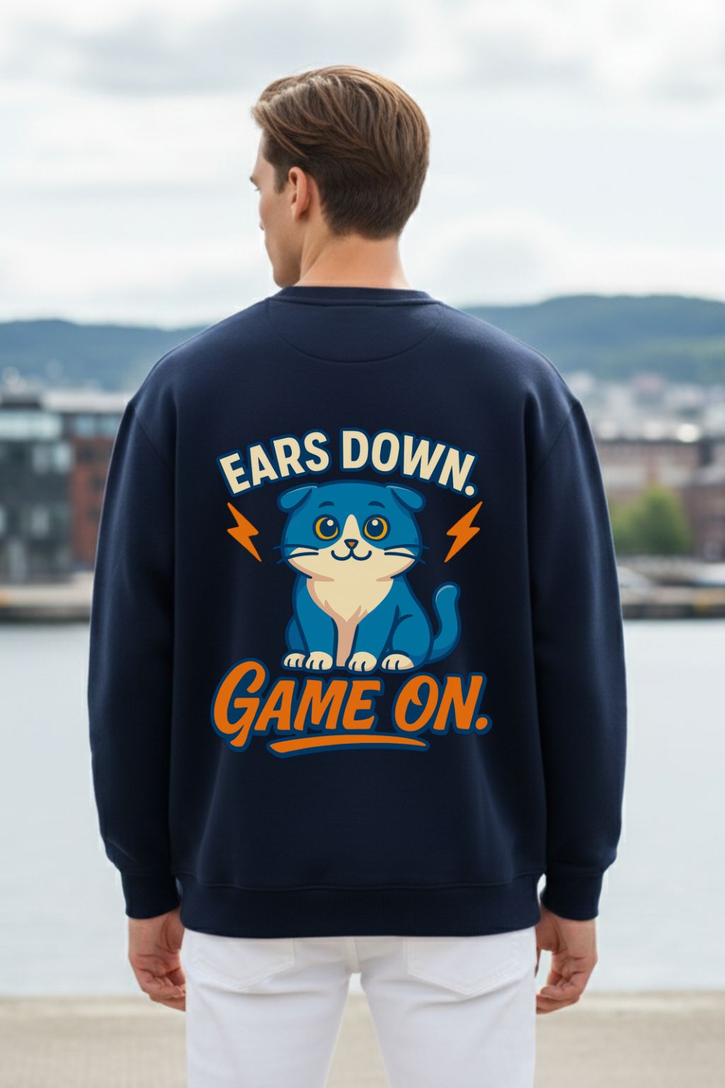 back view of a man wearing a navy blue oversized sweatshirt with a graphic and text, standing by a waterfront.