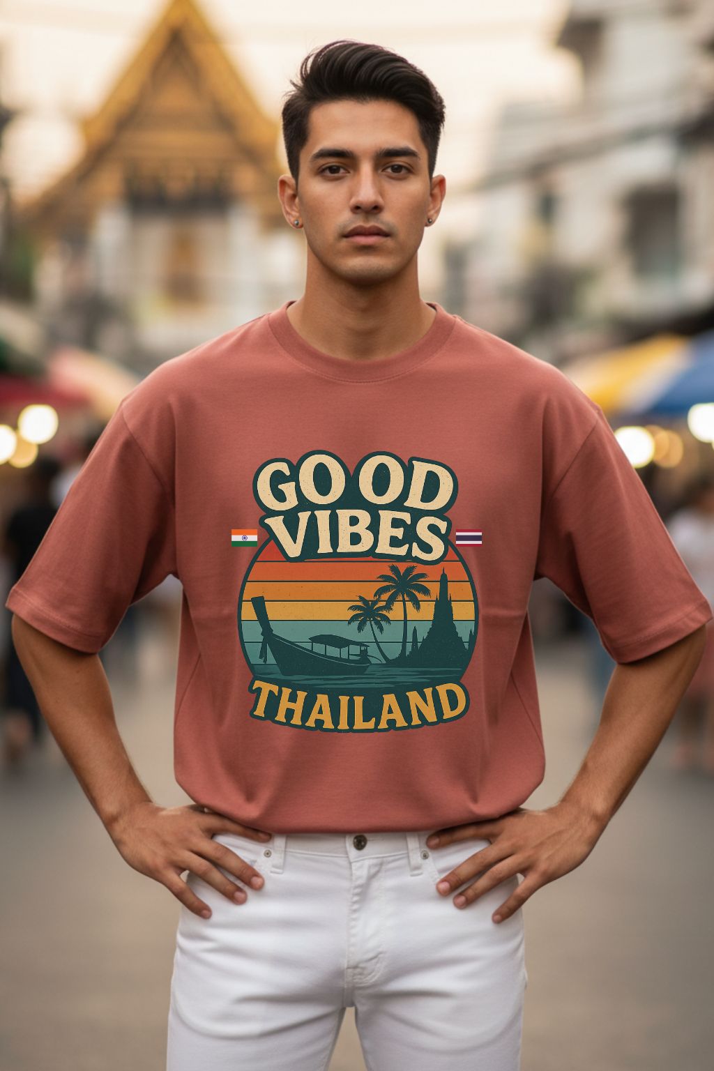 Man wearing a 'Good Vibes Thailand' coral oversized t-shirt with a blurred street background