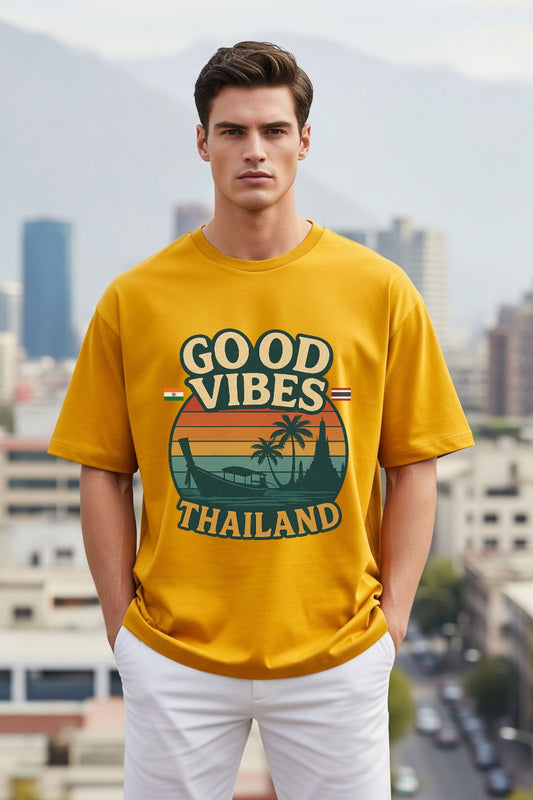 Man wearing a golden yellow oversized t-shirt with 'Good Vibes Thailand' design in an urban setting