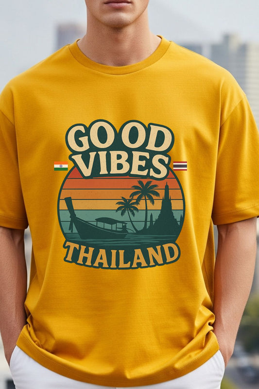 close up of a man wearing a golden yellow oversized t-shirt with 'Good Vibes Thailand' graphic design.
