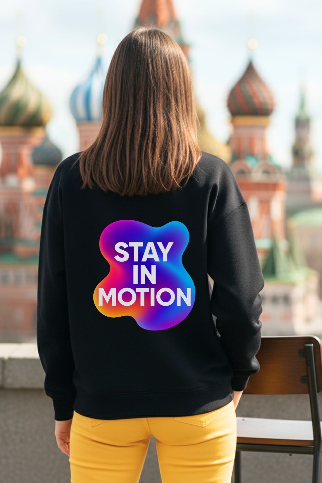 Woman wearing a black oversized sweatshirt with 'Stay in Motion' design, standing in front of a cityscape.