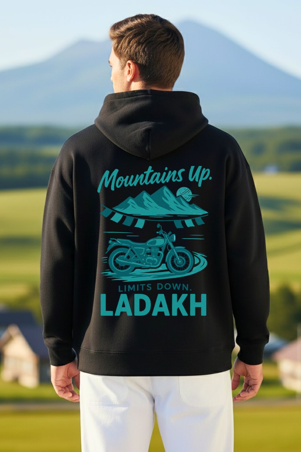 back view of a man wearing a black oversized hoodie with 'Mountains Up, Limits Down Ladakh' text and graphic in a scenic outdoor setting.