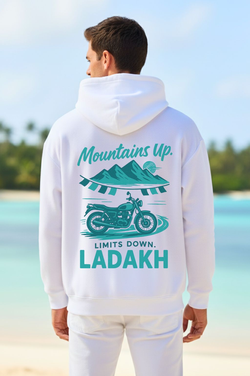 back view of a man wearing a white oversized hoodie with 'Mountains Up, Limits Down, Ladakh' design on a beach.