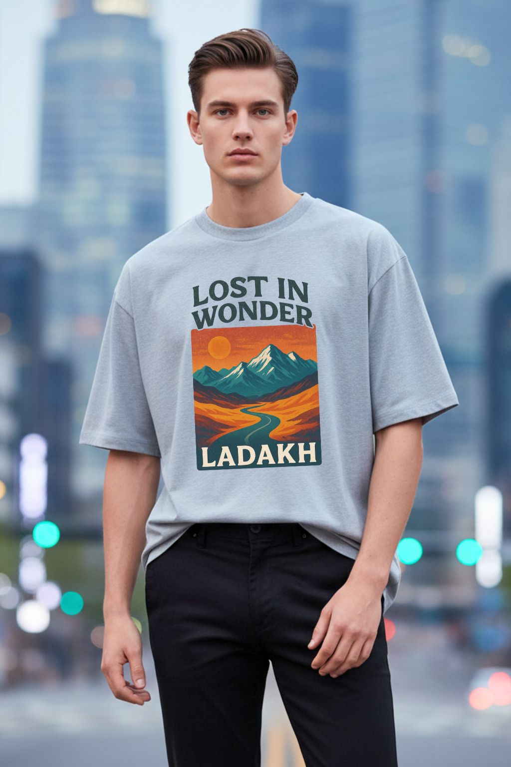 Man wearing a grey melange oversized  t-shirt with 'Lost in Wonder Ladakh' design against a cityscape background