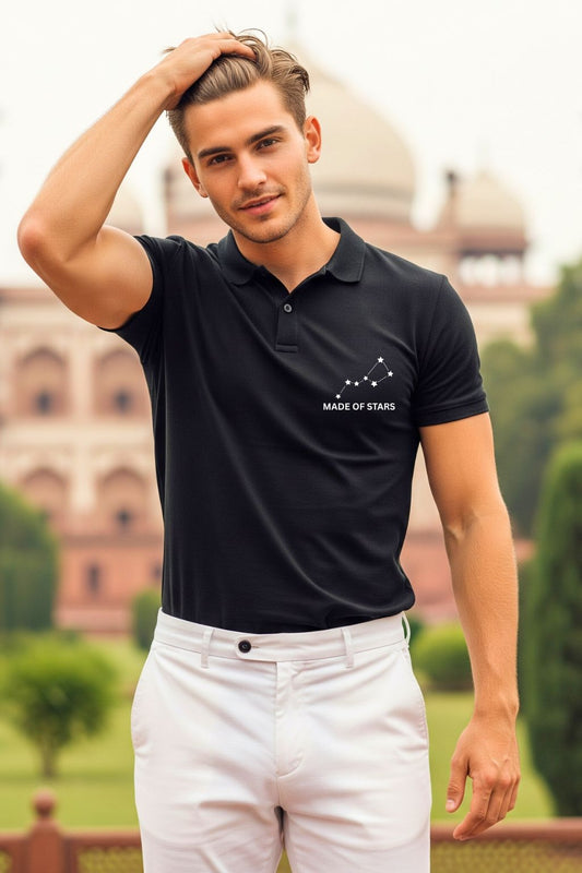 A handsome man wears a black ZUPPI 'Made of Stars' polo t-shirt, with one hand running through his hair. He stands tall, showcasing the t-shirt's front design in a stylish and confident pose