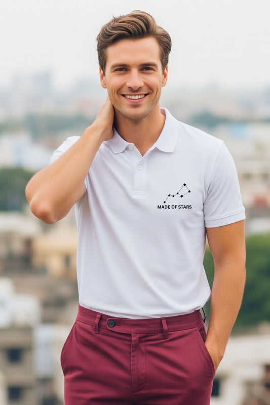A stylish man, viewed from the back, wearing a ZUPPI 'Made of Stars' white polo t-shirt featuring the 'Zodiac Mode: Always On' graphic. He is touching the back of his neck with one hand while the other is in his pocket.