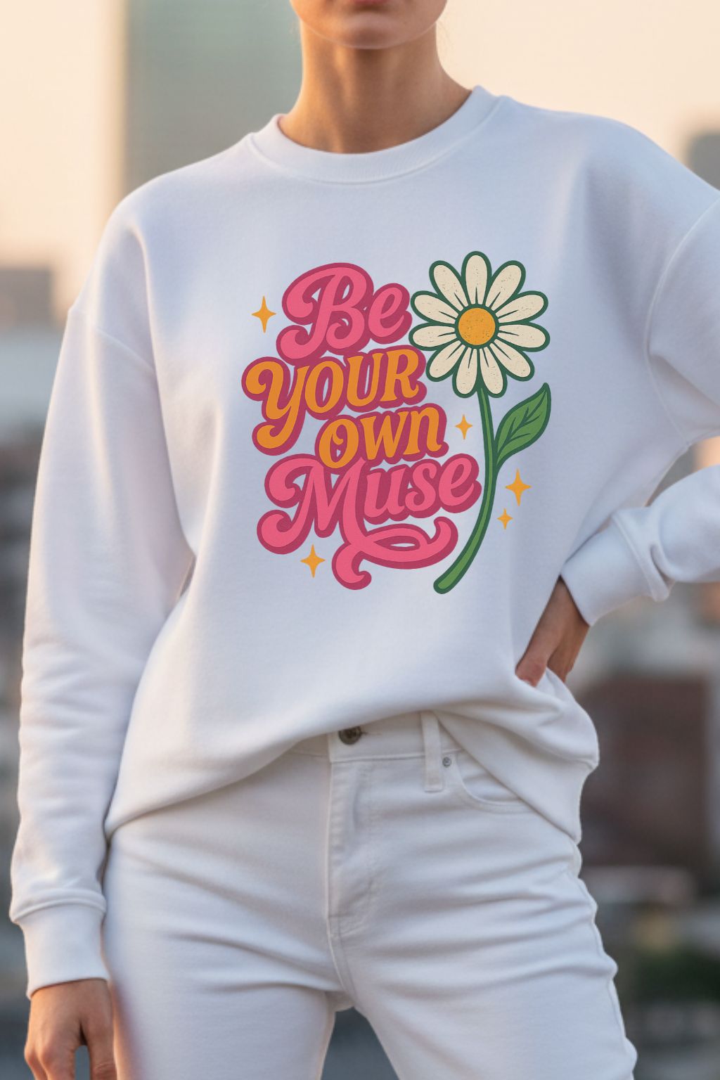 Woman wearing a white oversized sweatshirt with a colorful graphic and text 'Be Your Own Muse'.