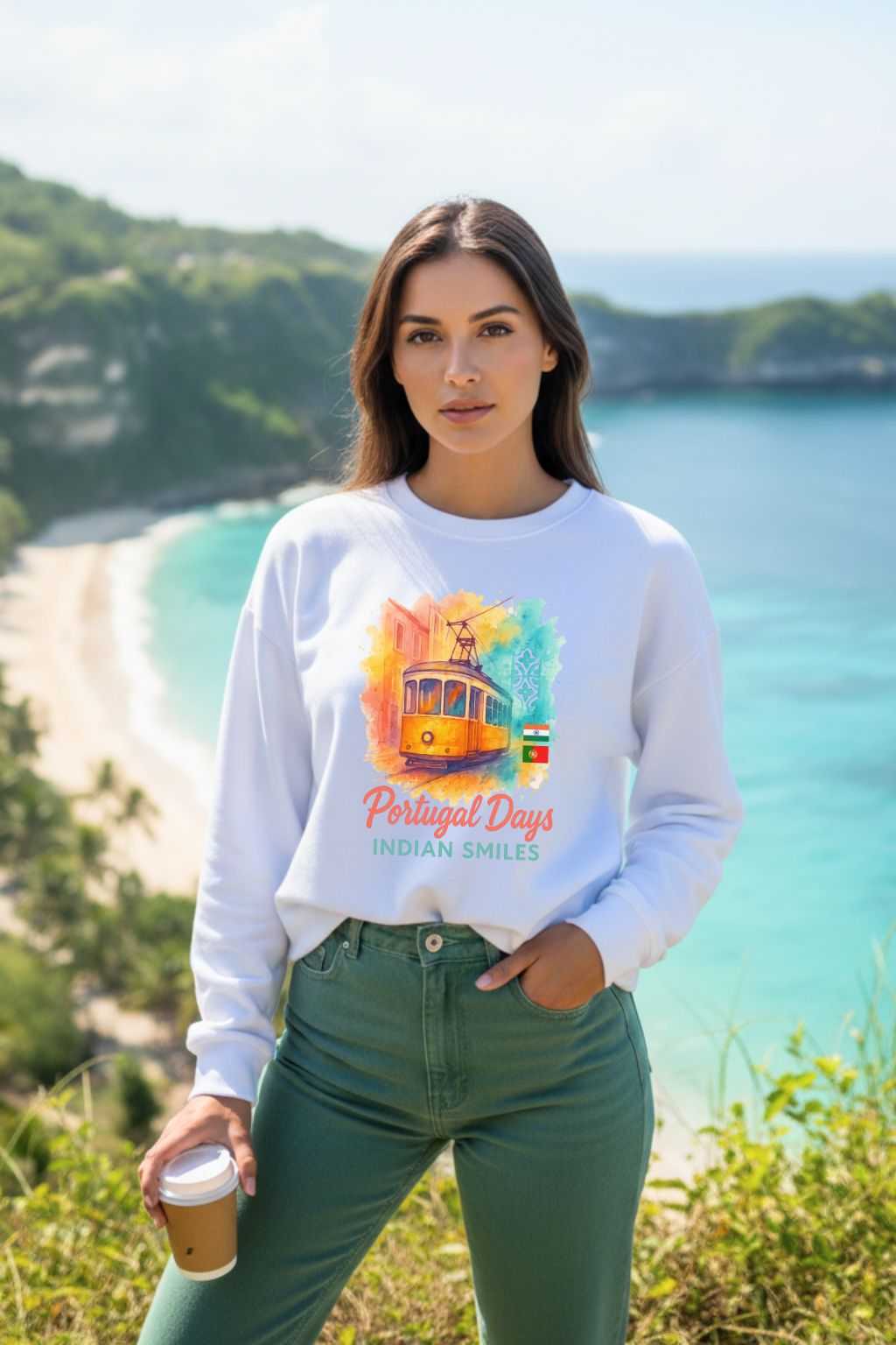 Woman wearing a white oversized sweatshirt with a colorful design, standing in front of a scenic beach.
