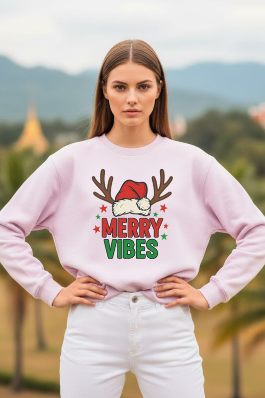 Woman wearing a light baby pink oversized sweatshirt with 'Merry Vibes' text and reindeer design outdoors.
