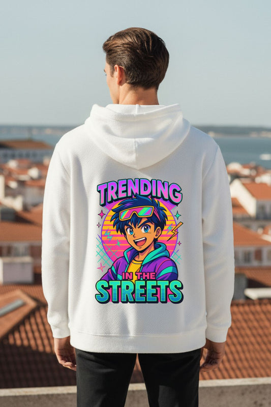 back view of a man wearing a white oversized hoodie with a colorful graphic and text on the back, standing on a rooftop with a cityscape view.
