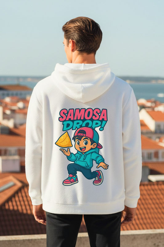 Man wearing a white hoodie with 'Samosa Drop!' graphic on the back, standing on a rooftop with a cityscape in the background.