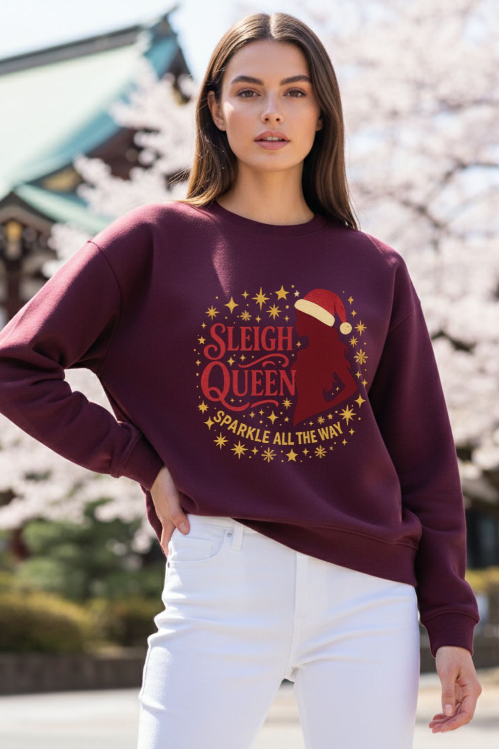 Woman wearing a maroon oversized sweatshirt with 'Sleigh Queen Sparkle All the Way' text and graphic, standing outdoors.