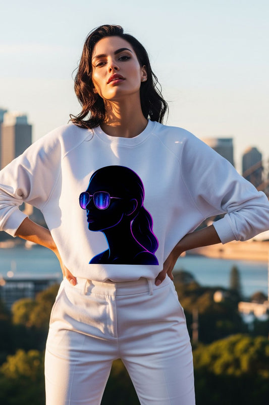 Woman wearing a white sweatshirt with a graphic design of a silhouette and sunglasses, standing outdoors with a cityscape in the background.